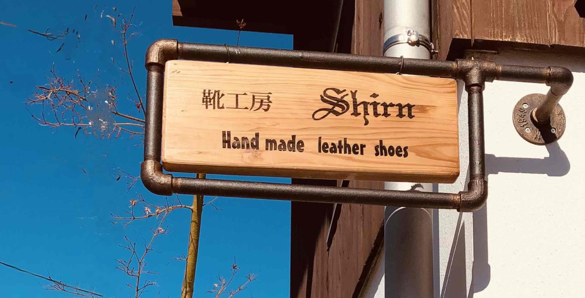青空の下に掛かる靴工房 Shirn の看板